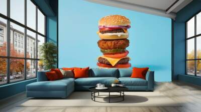 A triple-decker burger with sesame bun, grilled patty, cheese, tomato, fried patty, onion, and lettuce against a blue background. Wall mural