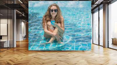 Beautiful long blonde wavy hair style woman model in bikini and sunglasses with cocktail at swimming pool. Wall mural