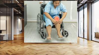 Fat woman sitting on wheelchair holding on her knee pain. Wall mural