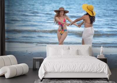 Happy smiling girl friends walking on the Beach together with hat, enjoying on the tropical beach, summer beach concept. Wall mural