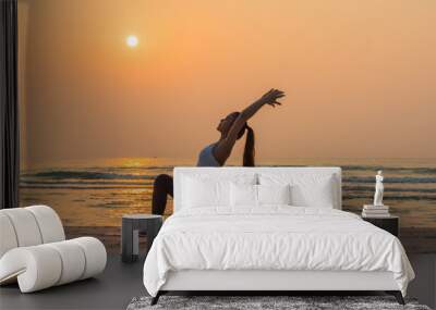 Silhouette young woman practicing yoga on the beach at sunrise.  Wall mural