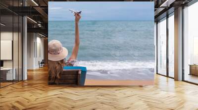 Summer beach vacation holidays trip concept, Happy young Asian woman with hat relaxing on beach chair and holding airplane model flying over blue sky. Wall mural