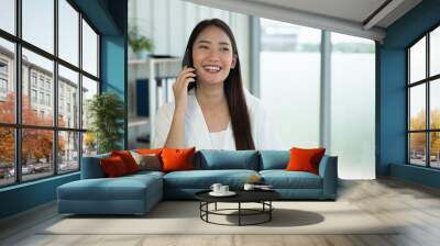 Young Asian woman talking on mobile phone with happily. Wall mural