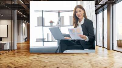 Image of a young beautiful Asian Business woman smiling while working with a laptop and talking to work doing math finance on an office desk, tax, report, accounting, statistics, and research concepts Wall mural