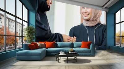 Two good-looking Asian Muslim women, hello, greeting, and Quran at the wooden table at his house during the night during the month of ramadan, Arabic calligraphy meaning Al Quran. Wall mural