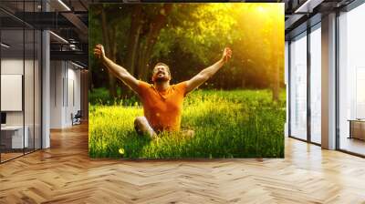 A happy man is relaxing on green grass with squint eyes  Wall mural