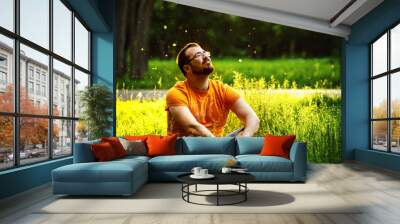 A happy thoughtful dreamer man is sitting on green grass  Wall mural