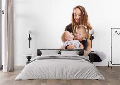 Concept of healthy happy family. Mother is sitting on floor with two cute children isolated at white background. Wall mural