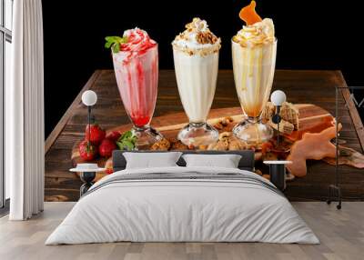 Three sweet milkshakes with nuts, caramel, strawberry and whipped cream at a wooden board on table background. Wall mural