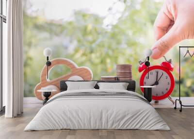 Close up hand arranging red alarm and wooden toy car on stack of coins. The concept of saving for car. Wall mural