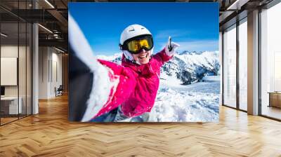 Selfie snowboarder. Young happy woman taking selfie with the smartphone on the top of the mountain Wall mural