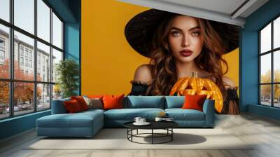 Portrait of magician woman wearing witch costume and halloween makeup holding a carved pumpkin. Wall mural