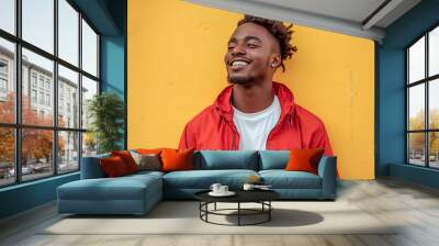 Smiling cool stylish young black African man wearing white t-shirt, red jacket standing outdoor with yellow cement wall background. Wall mural