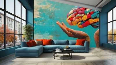 A colorful yarn brain is held in the cupped palms of two hands against a blue background. Wall mural