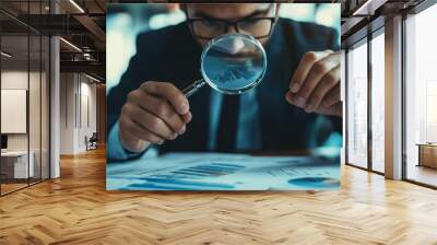 Close-up of a businessman in a suit looking at a document with a magnifying glass. Wall mural