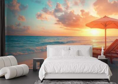 Two lounge chairs under a beach umbrella on a sandy beach at sunset with the ocean in the background. Wall mural