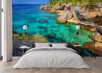 Beautiful clear turquoise water near rocks and cliffs in Negril Jamaica. Caribbean paradise island and water at the seaside with a blue sky and nice day light Wall mural