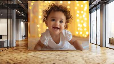 A cute baby girl with curly hair is smiling and crawling on the bed, wearing white short sleeves. Portrait of a happy black child playing on the floor on light white blurred flare colorful background Wall mural