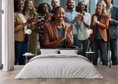 A group of business people are clapping and celebrating with one woman in a wheelchair. The modern office space shows a diverse group of employees standing around lady in the wheelchair cheering her Wall mural