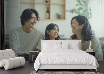 A young Japanese couple and their daughter, all smiling at the camera. Loving mother and father with kids enjoying time together at home sofa Wall mural