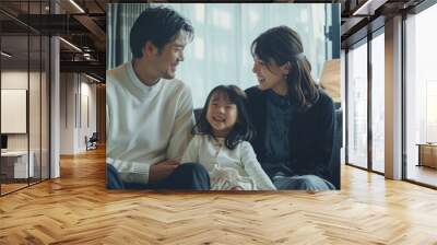 A young Japanese couple and their daughter, all smiling at the camera. Loving mother and father with kids enjoying time together at home sofa Wall mural