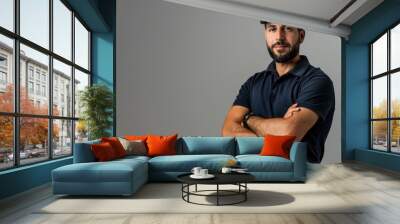 Attractive male service technician worker wearing a navy blue polo shirt and hat, standing with his arms crossed on a grey background Wall mural