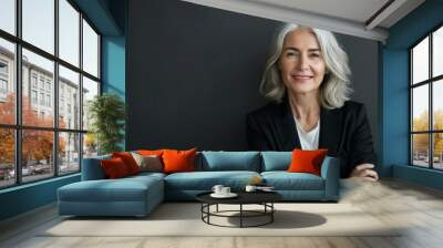 Elegant middle-aged woman with shoulder-length silver hair, smiling and standing confidently in front of the camera against a black background. senior woman Wall mural