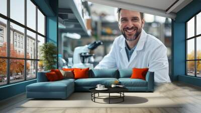 Handsome male scientist in a white lab coat looking at the camera and smiling while working with a microscope. Technician worker. Blood work or health service Wall mural