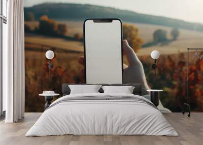 Mockup of a blank smartphone, mobile phone screen held in hand, countryside background. Wall mural