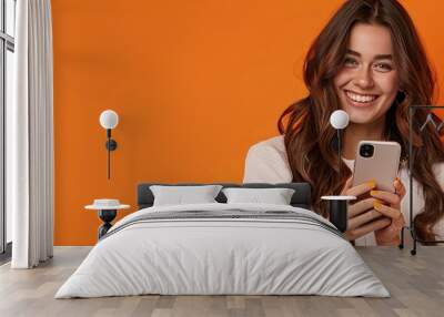 Photo of An elegant young woman in her 20s with long wavy hair, happy smiling while using an mobile phone on a orange and black background with copy space for text or product. Web banner. Wall mural