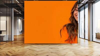 Photo of An elegant young woman in her 20s with long wavy hair, happy smiling while using an mobile phone on a orange and black background with copy space for text or product. Web banner. Wall mural