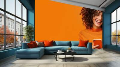 Portrait of smiling african american woman using smartphone isolated on orange background, wearing red sweater with copy space for your text message or promotion banner. Wall mural