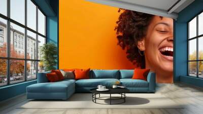 Woman with curly hair laughing while holding her phone against an orange background, banner ad. Web design template with copy space. african american woman smartphone isolated on orange background Wall mural