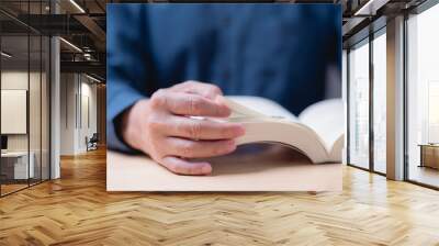 Reading and learning book concept. A man is reading a book with his hand on the page. The book is open to a page with a picture of a person Wall mural