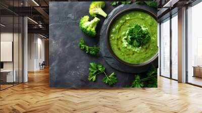 Vibrant green broccoli soup in a bowl on a dark background with ingredients, in a top view Wall mural