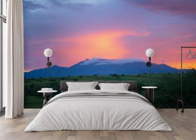 Distant mountain range with foggy top at sunset with green fields. Wall mural