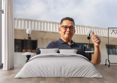 A self made middle aged asian entrepreneur and businessman making a thumbs up sign, posing in front of his factory or warehouse facility. Wall mural