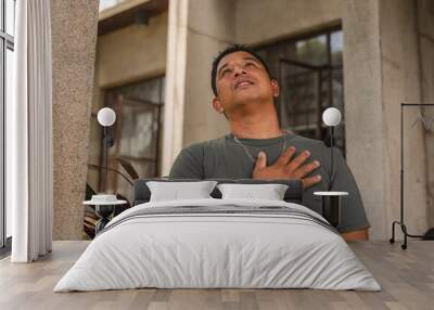 Middle aged Asian man looking up with hand on chest, expressing faith and spirituality Wall mural