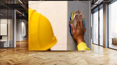 Over-the-shoulder view of a construction worker in a yellow hard hat meticulously cleaning a marble wall with a wash cloth. Finishing works. Wall mural