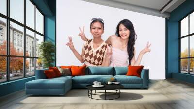 Two cute young asian women make peace signs. Close friends posing together. Isolated on a white background. Wall mural