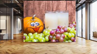 Two glasses of white stum with some green and red grapes and a funny pumpkin photographed in front of a wooden wall. Wall mural