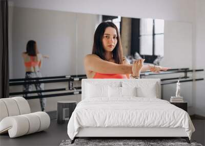 Portrait of fit sporty young woman doing stretching over gym room background. Healthy life, keep fit concepts. Portrait of a young girl at a fitness training centre. Wall mural