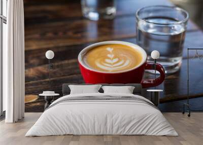 Water and red cup of coffee with latte art on wooden background. Table in cafe. Concept of easy breakfast. Small ceramic cup and glass Wall mural