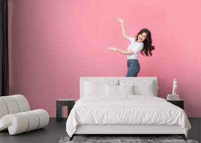 An asian woman in a casual outfit hopping off with her arm presenting, a cheerful expression on her face as she is excited to present something in isolated pink background. Wall mural