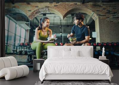 Asian couple healthy eating salad after exercise at fitness gym. Asian man and woman eating salad for health together. Wall mural