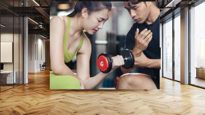 Asian female workout training lifting dumbbell with professional trainer. Asian man trainer coach helping woman bicep exercise with dumbbell in fitness gym. People active in healthy lifestyle. Wall mural