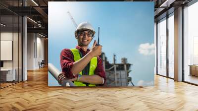 Asian young engineer glasses smiling wear a safety helmet equipment and drawing on hand with radio communication. Wall mural