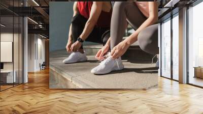 Close up hand of active young man and woman tying shoelace on her running shoes. Preparation before jogging exercise. Fitness and sport activity. Healthy exercise concept. Wall mural