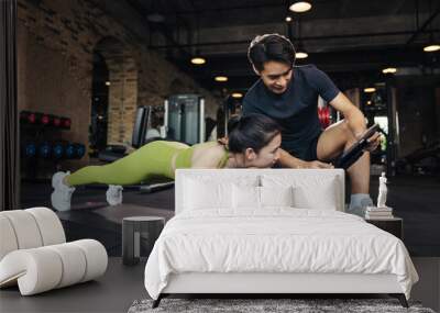 Personal trainer looking at digital tablet and explaining progress to young woman at the fitness gym. Asian man trainer coach helping young female planking exercise for beaultiful building slim body. Wall mural