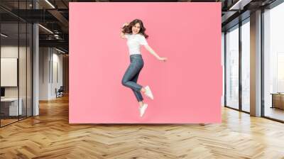 Young Asian woman in a white t-shirt cheerful expression on her face as she is very happy over something excited smile and jumping with her arm raised in air on isolated pink background. Wall mural